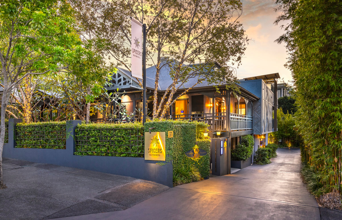 Spicers Balfour's heritage Queenslander at dusk, lit up behind its leafy hedge on Balfour Street, New Farm