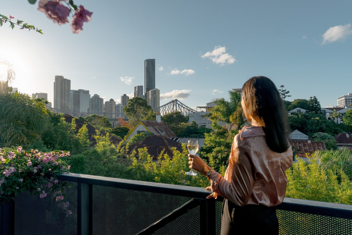 Guest with a glass of wine on the rooftop at Spicers Balfour, looking over New Farm to the Brisbane skyline and Story Bridge